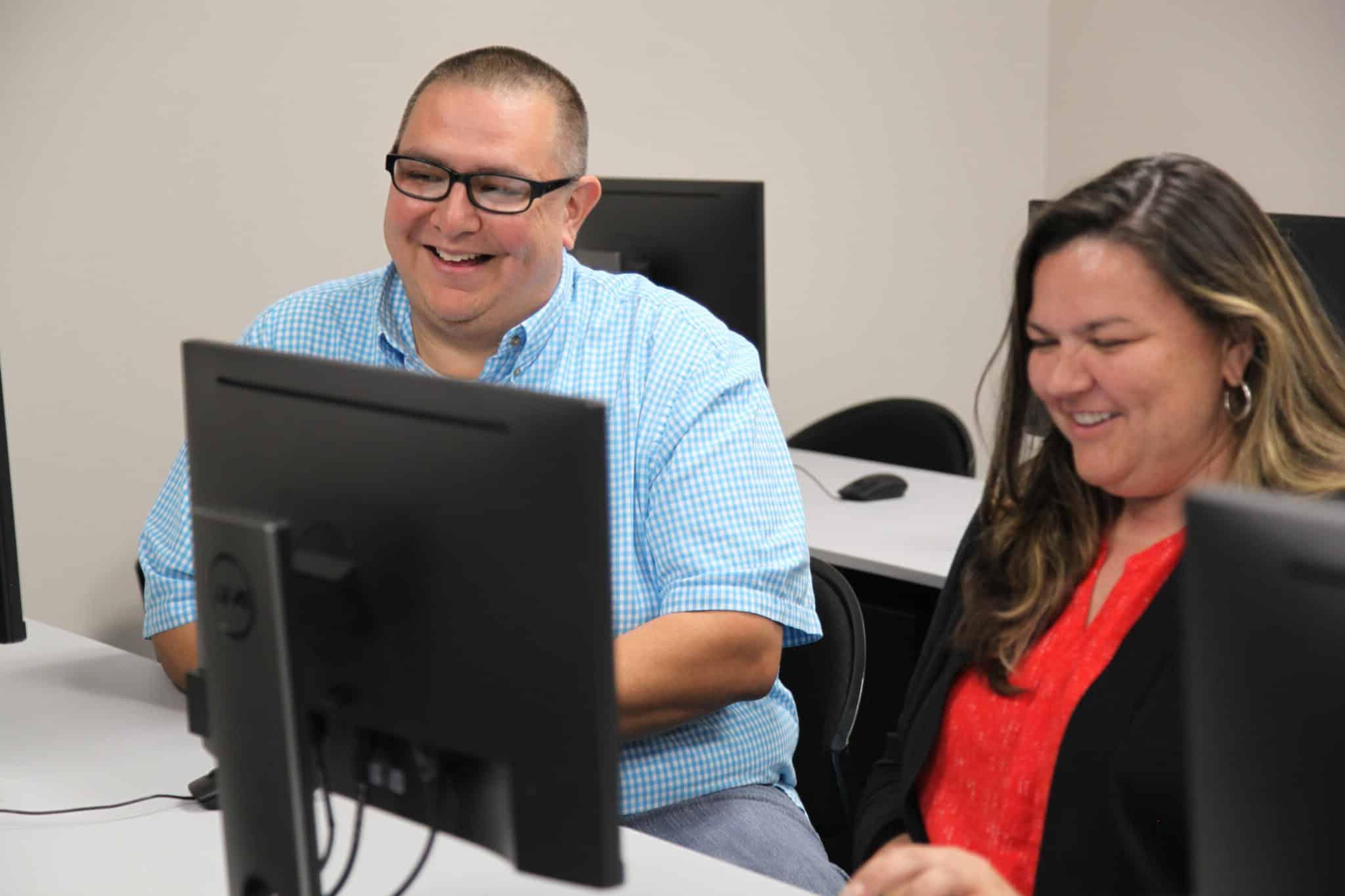 Two colleagues at Howard Payne University laughing and enjoying a moment at their computer workstations. | HPU