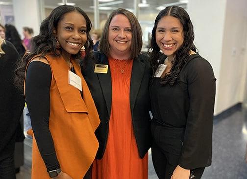Three smiling women in professional attire with Howard Payne University name tags at an indoor event. | HPU